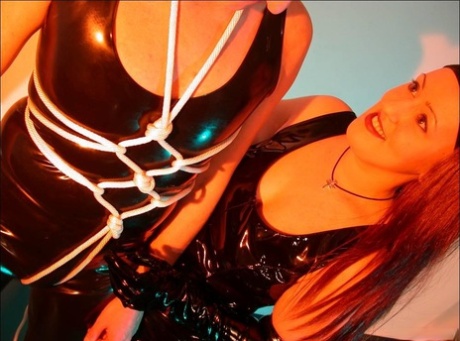 Redheaded domme restrains a male slave while wearing black latex attire 50703337