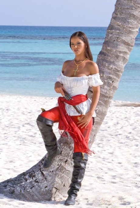 Female pirate puts down her pistol to pose naked on a sandy beach 76923771